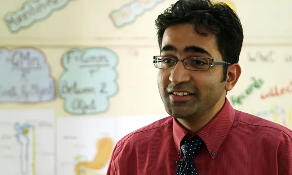 Headshot of a young Indian man with brown hair and glasses in a shirt and tie