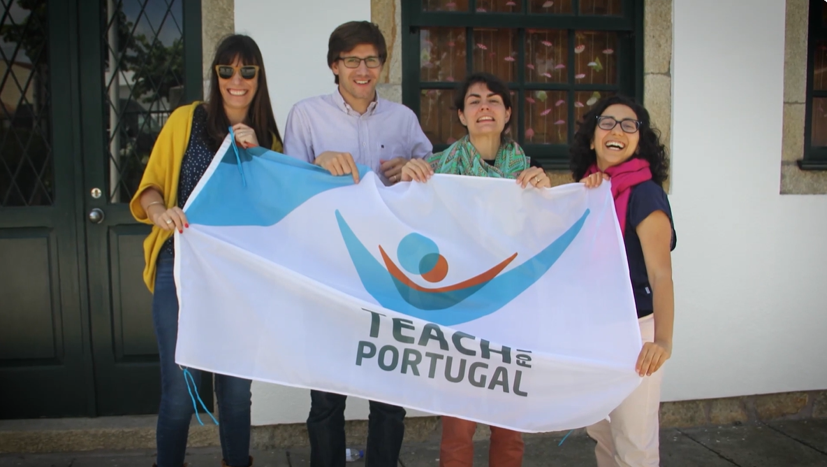 A man and three women, all white with brown hair, smile while holding a flag that says Teach For Portugal