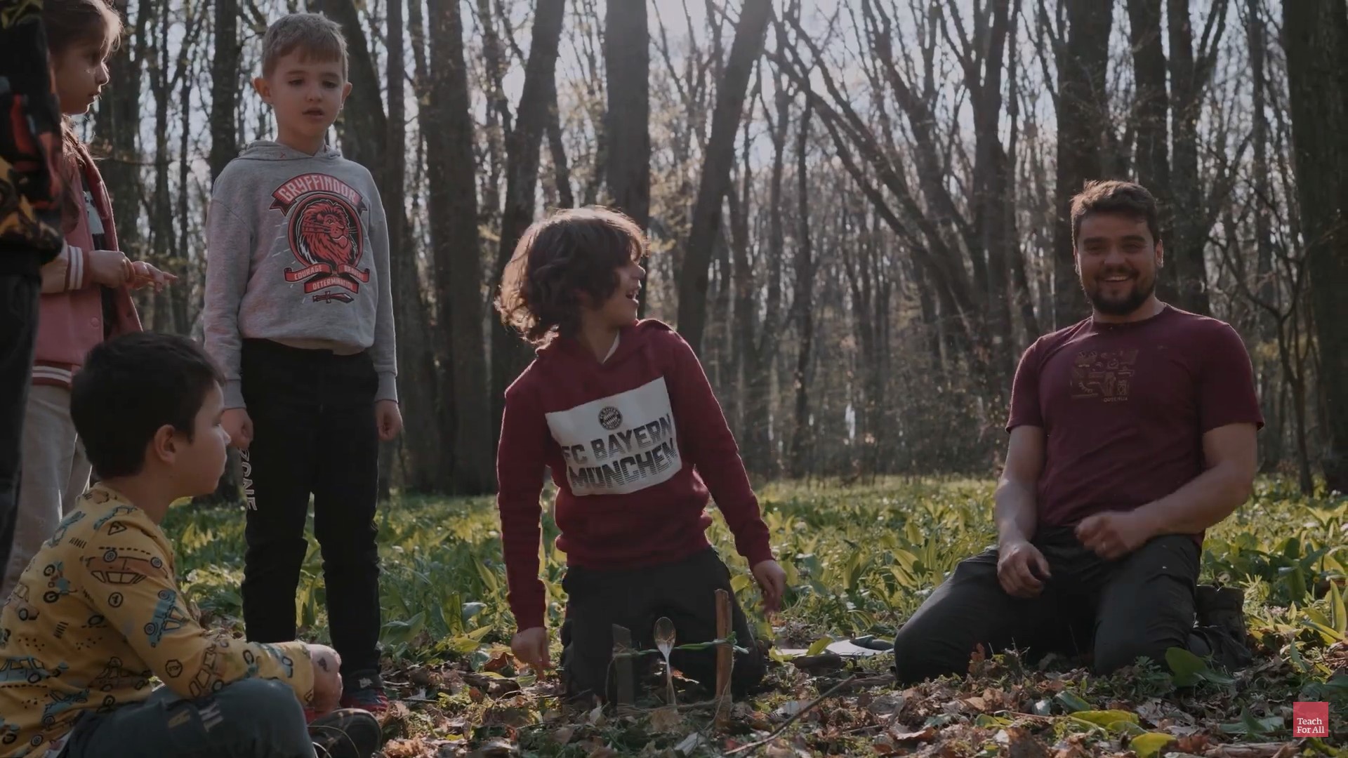 Three children and a young man with a beard are out in the woods smiling