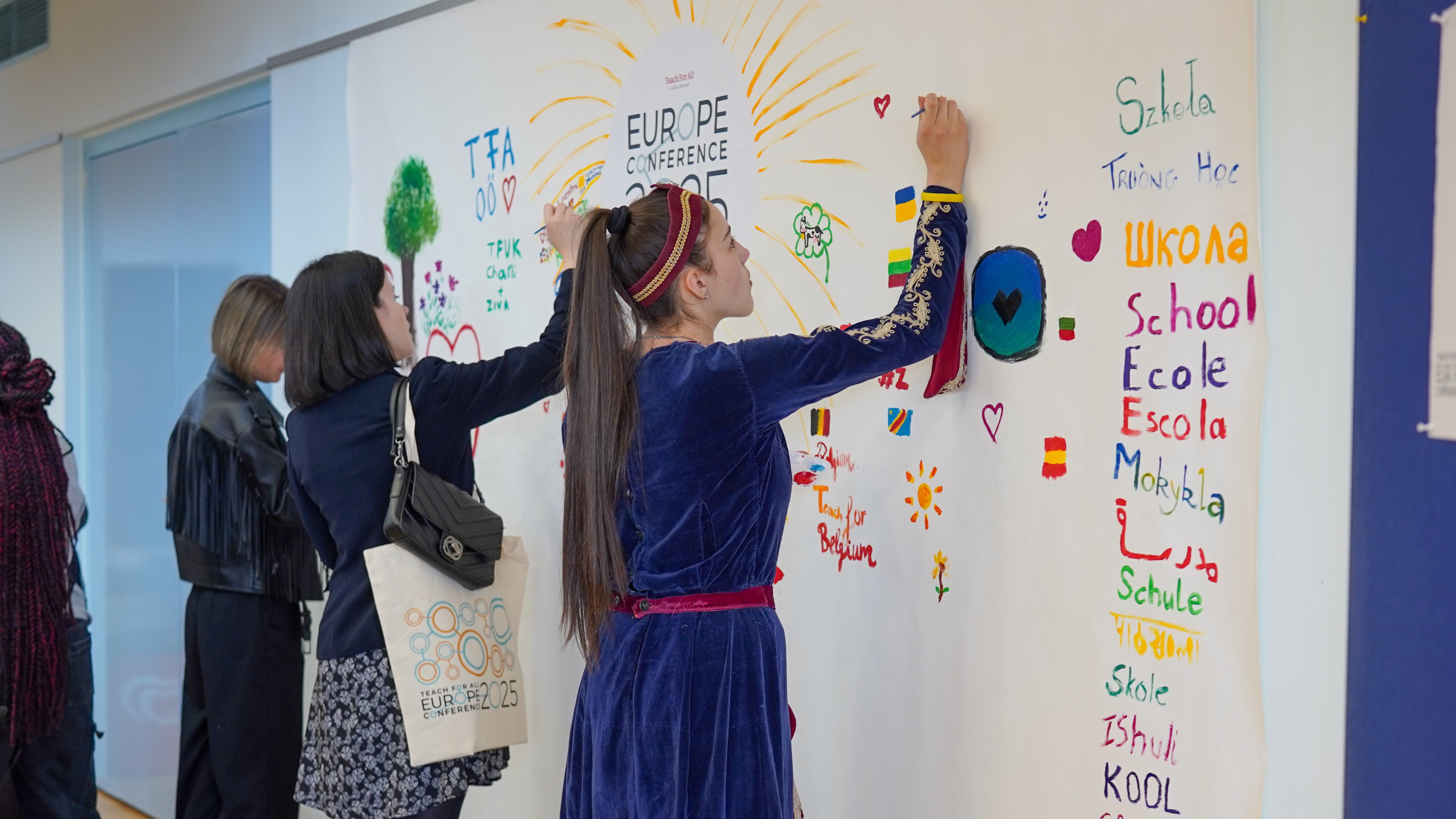 A young woman with a ponytail writes in marker on a wall that says Europe Conference and is covered in brightly colored writing and drawing