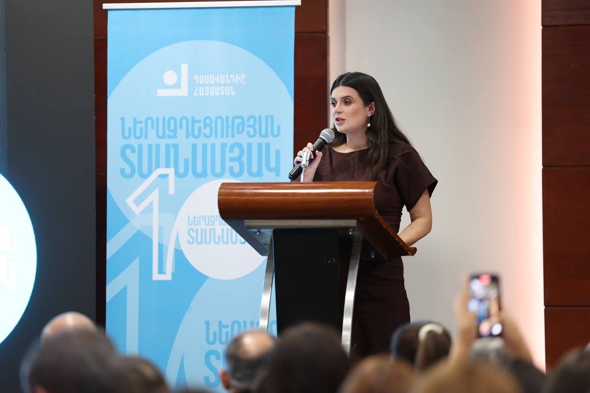 A young white woman with long brown hair speaks into a microphone