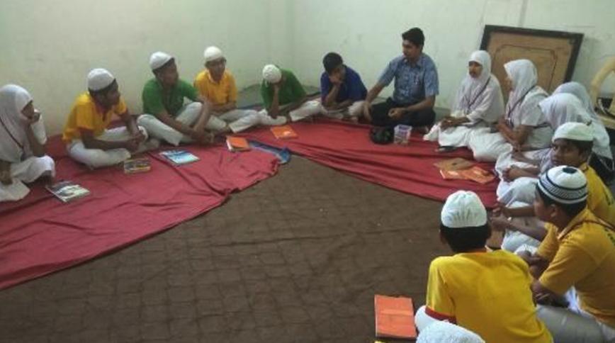 Teacher seated on floor with thirteen children wearing white head covering