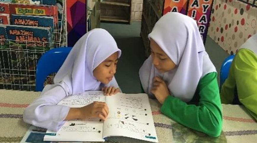 Two Malaysian girls looking down at an open book with pitures and words