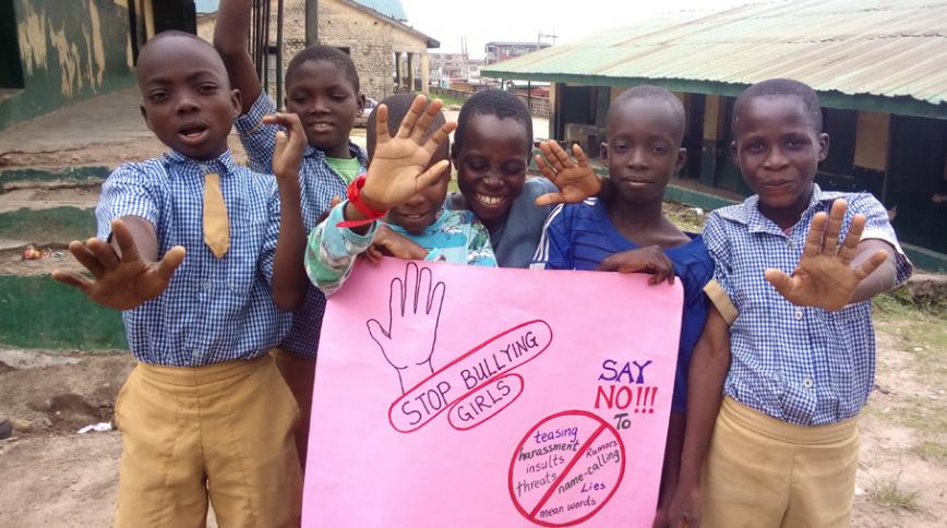 Six boys in blue shirts holding a pink, handmade sign with the words "STOP BULLYING GIRLS"