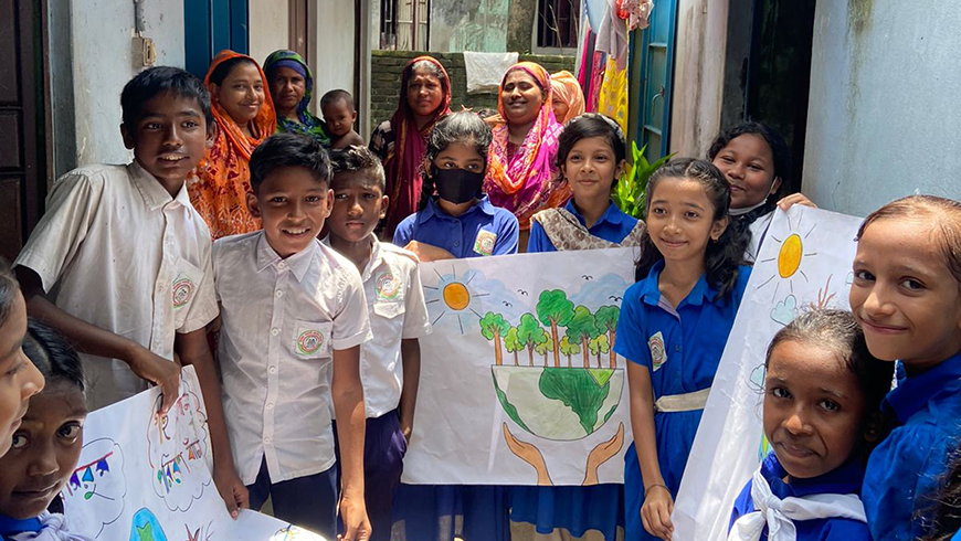 Students and community members pose in front of houses with climate awareness posters they have made