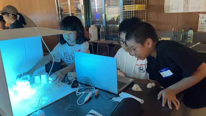 Three Asian children experiment with a light box and computer